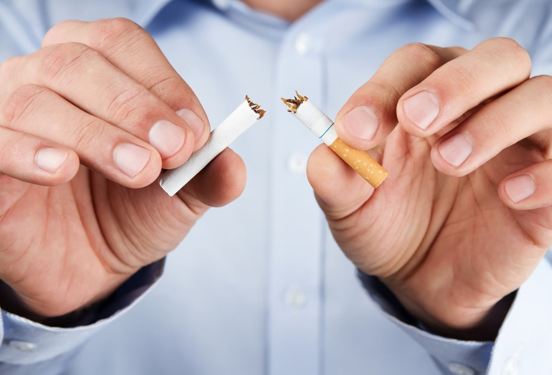Ein Mann hält eine in zwei Teile gebrochene Zigarette in der Hand. Er möchte mit dem Rauchen aufhören.